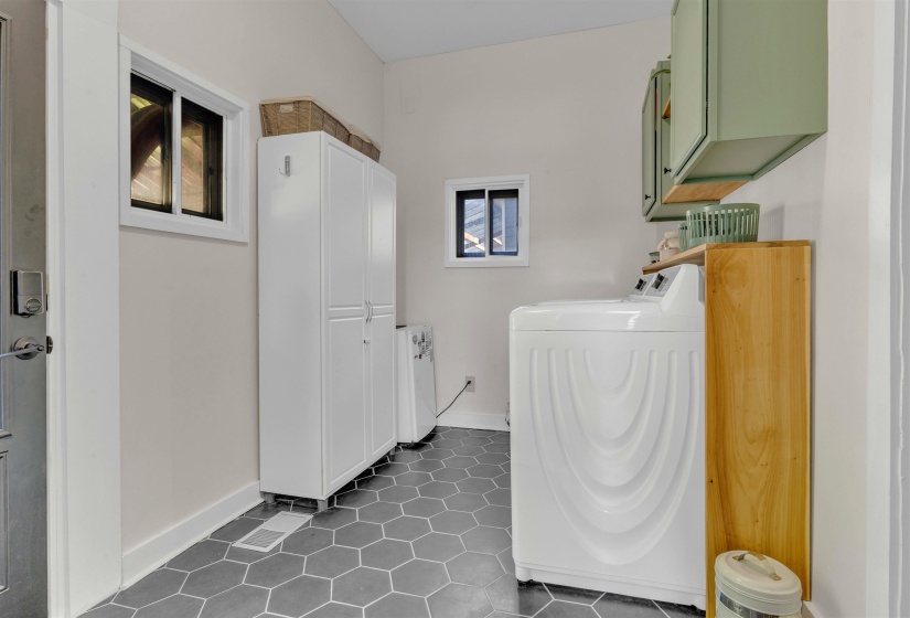Laundry area featuring hexagonal tile flooring, white shaker-style cabinetry, two windows, and light green wall-mounted storage cabinets