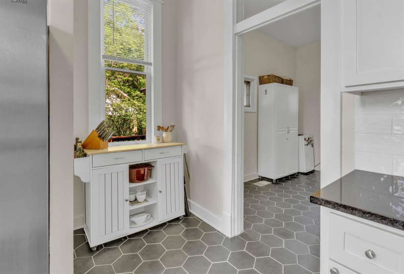 Kitchen space featuring hexagonal floor tiling, a white cabinetry installation with dark countertops, and a full-height window