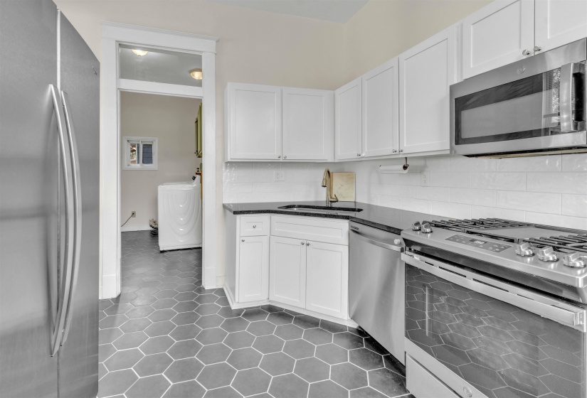 Kitchen featuring hexagon tile flooring, white shaker cabinetry, stainless steel appliances, dark countertops, and a white subway tile backsplash