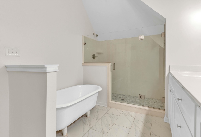 Bathroom featuring a freestanding soaking tub, glass-enclosed shower with pebble-style flooring, white tile flooring, and a vanity with a white countertop and base cabinetry