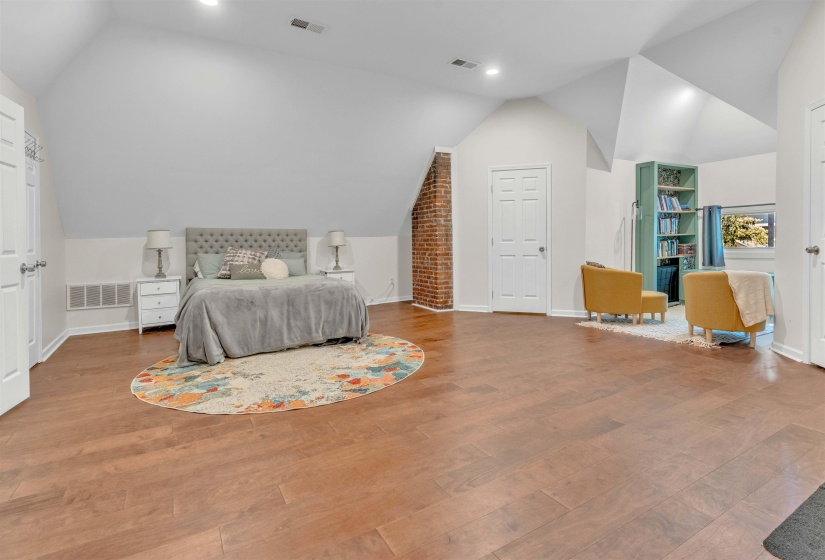 Spacious room featuring wood-finish flooring, vaulted ceilings, recessed lighting, and a visible brick accent wall