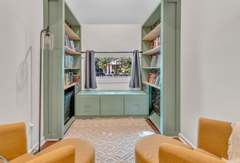 Built-in shelving units in a soft green finish frame a window with an integrated window seat featuring three storage drawers
