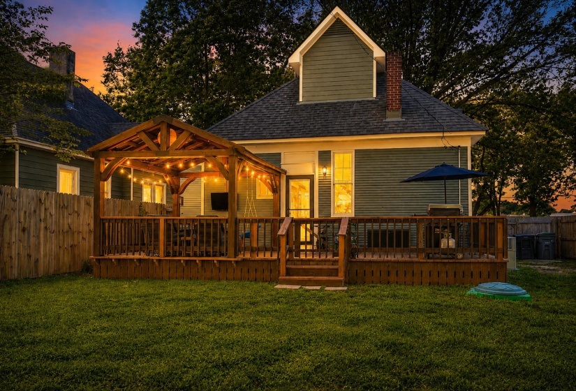 Expansive backyard featuring a multi-level wood deck, a covered wood gazebo with string lighting, a manicured lawn, and a privacy fence