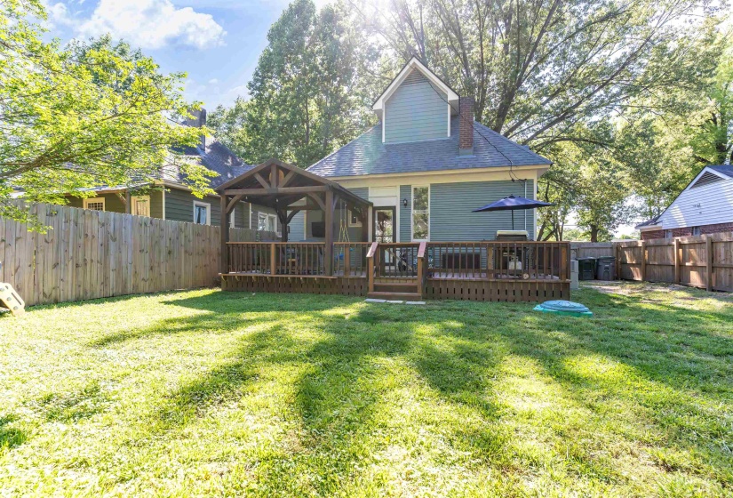 Expansive backyard featuring a wood privacy fence, a multi-level wood deck, a covered gazebo, and a light blue exterior with a dormer window