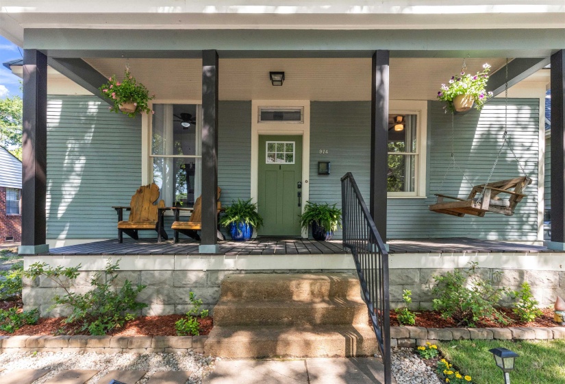 Covered front porch featuring a green entry door with window pane detailing, black railing, and plank flooring