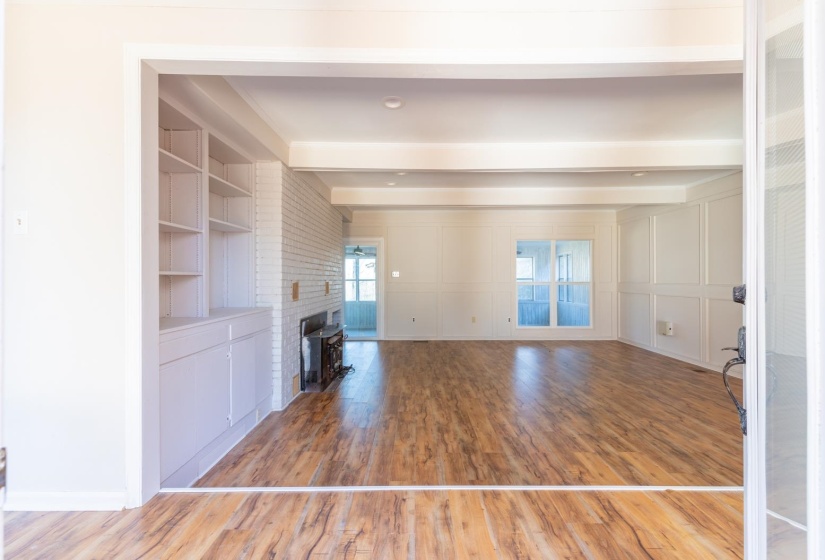 Unfurnished living room with light wood-type flooring, a decorative wall, beamed ceiling, a fireplace, and built in shelves