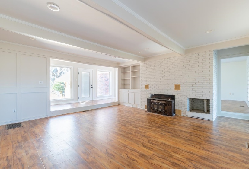Unfurnished living room with a brick fireplace, hardwood / wood-style floors, built in features, ornamental molding, and beamed ceiling