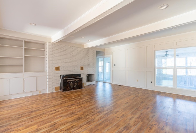 Unfurnished living room with a decorative wall, wood finished floors, a brick fireplace, built in shelves, and crown molding