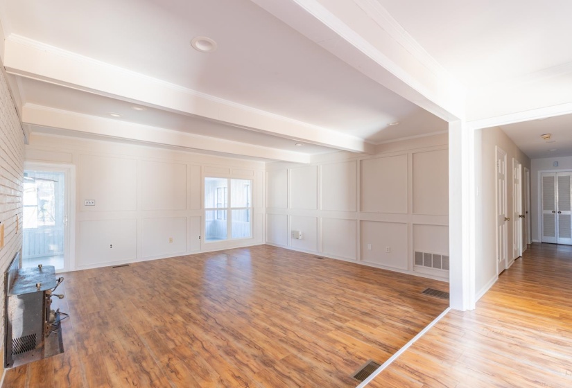 Unfurnished living room with a decorative wall, light wood finished floors, beamed ceiling, and a fireplace