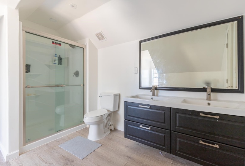 Full bathroom featuring double vanity, a shower stall, light wood-style floors, and vaulted ceiling