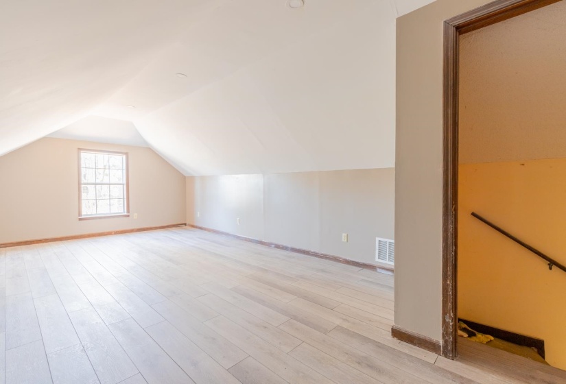 Additional living space with light wood-style floors and lofted ceiling