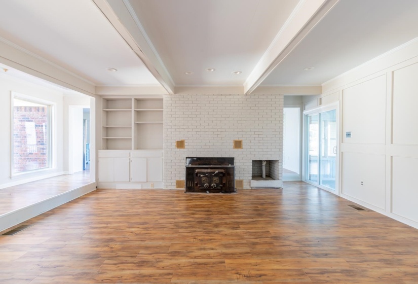 Unfurnished living room with a fireplace, light wood-style floors, beamed ceiling, built in shelves, and a decorative wall