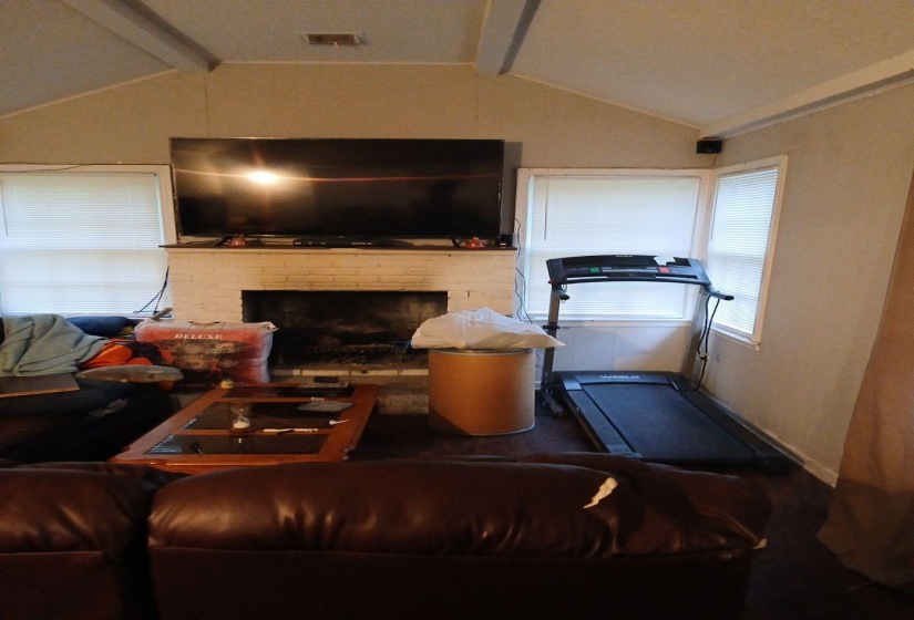 Living area featuring a brick fireplace with a mantle, vaulted ceilings, and multiple windows. Possible 3rd bedroom