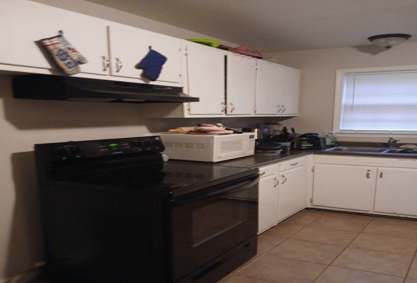 Kitchen featuring a black electric range, white cabinetry, dark countertops, a stainless steel sink, and tiled flooring