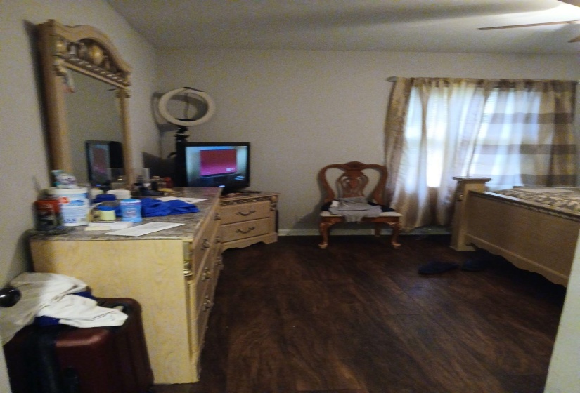 Wood-finish flooring provides a rich foundation for this room, featuring light-toned walls and a window with sheer and patterned curtains