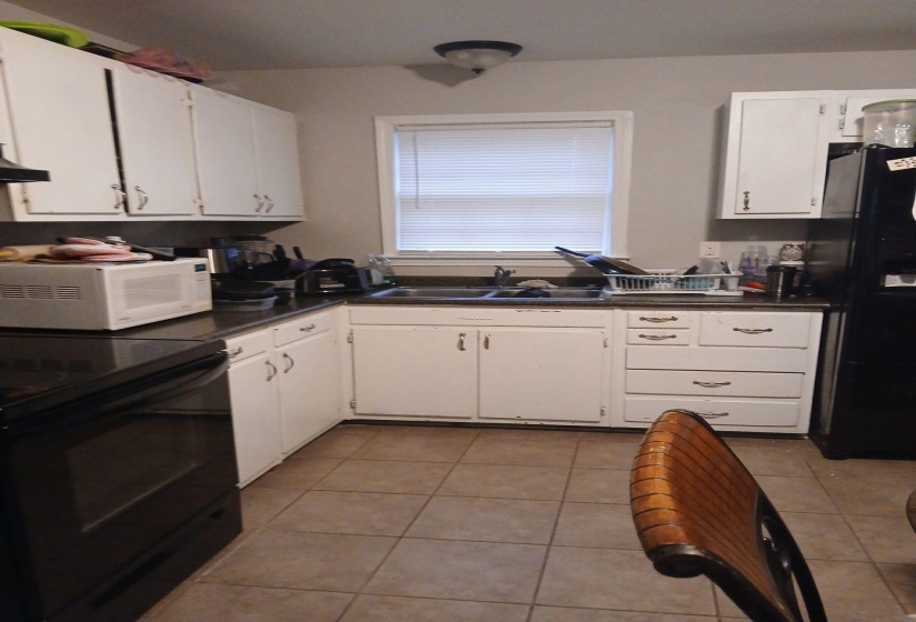 Kitchen featuring white cabinetry, dark countertops, a window with blinds, a double basin sink, and tile flooring