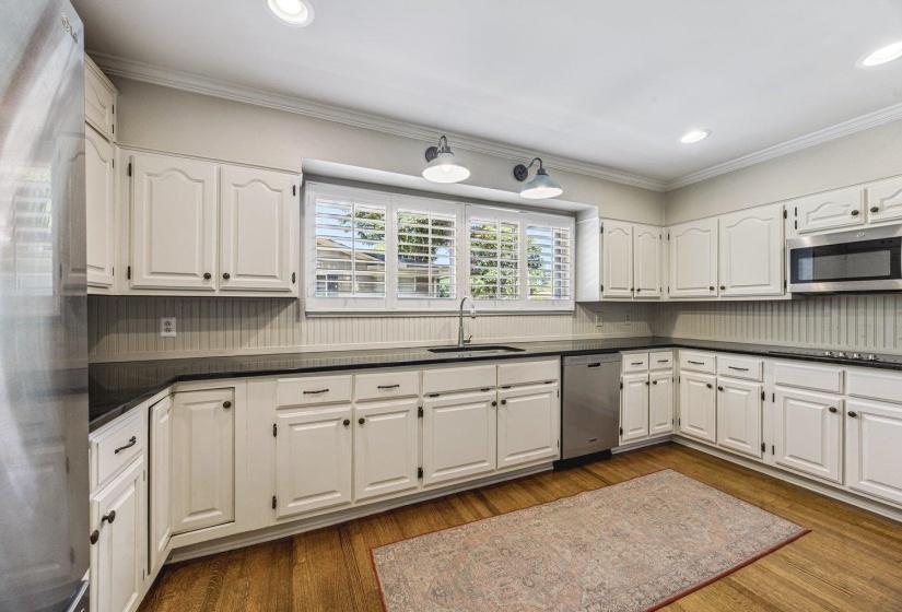 Spacious kitchen featuring extensive white cabinetry, dark countertops, beadboard backsplash, stainless steel appliances, and wood-finish flooring