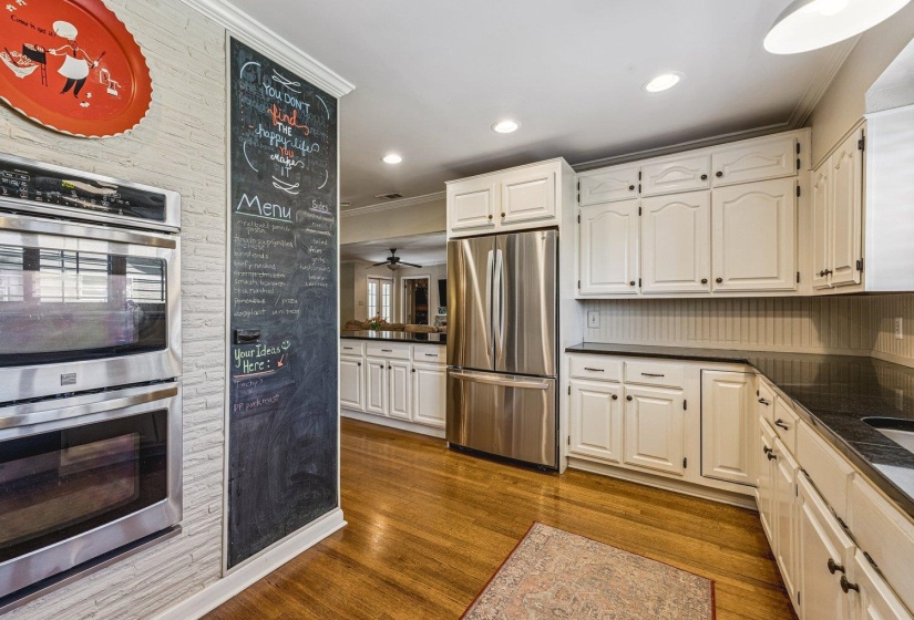 Kitchen featuring hardwood flooring, white cabinetry with dark hardware, stainless steel French door refrigerator, built-in double oven, and dark countertops