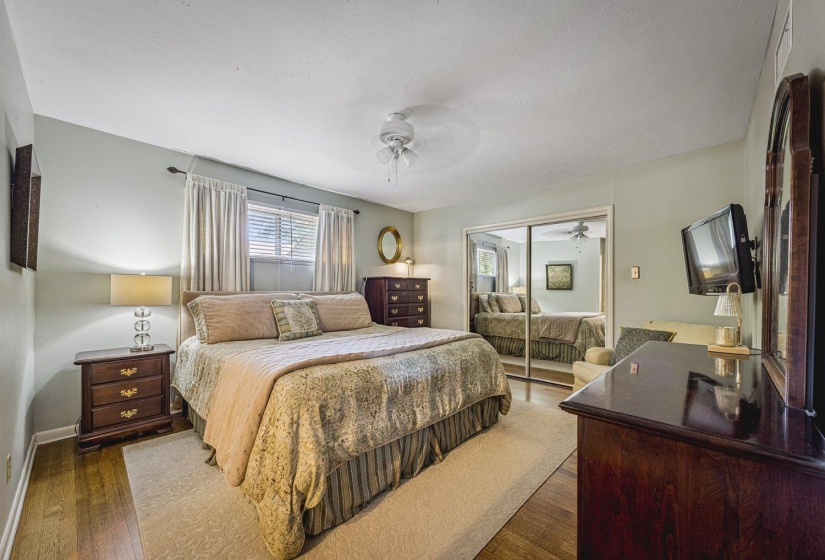 Bedroom featuring wood-finish flooring, a ceiling fan, a window with blinds and drapes, and a mirrored closet