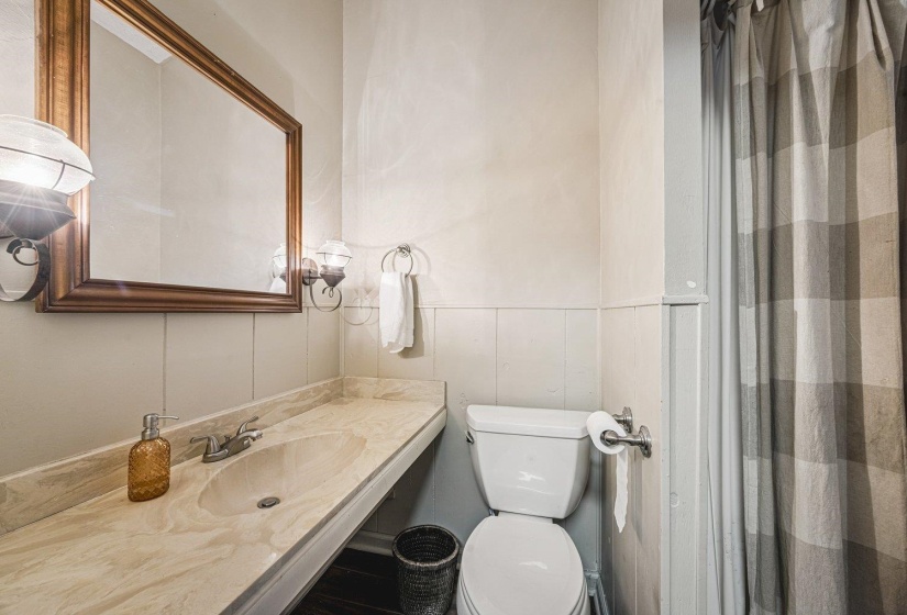 Bathroom featuring a stone-look countertop with an integrated sink, a large framed mirror, vanity lighting, wainscoting, and dark wood-finish flooring