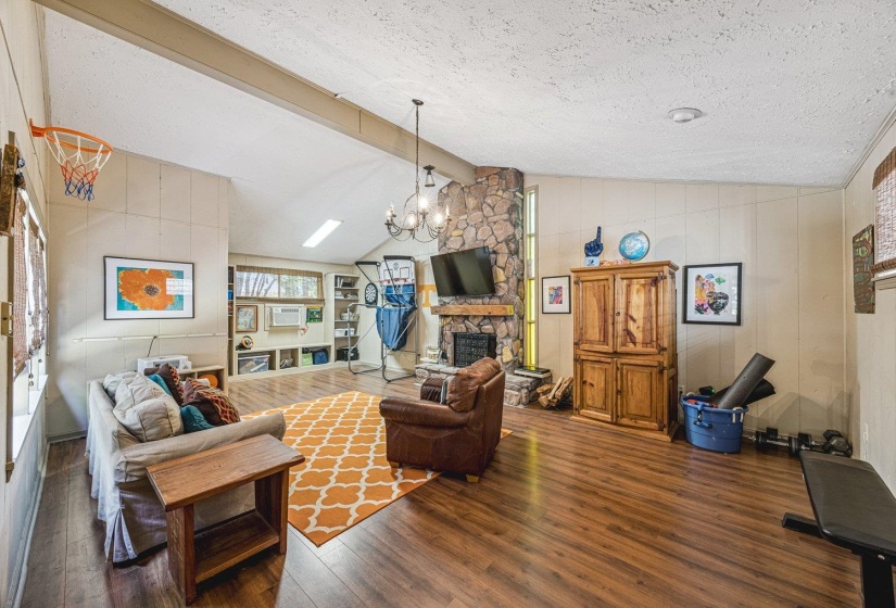 Spacious living area featuring wood-finish flooring, a prominent stone fireplace, and a vaulted ceiling with exposed beam