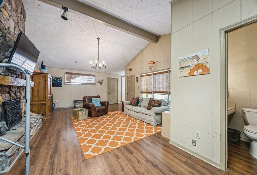 Living area featuring wood-finish flooring, a stone-clad fireplace, and a vaulted ceiling with exposed beam