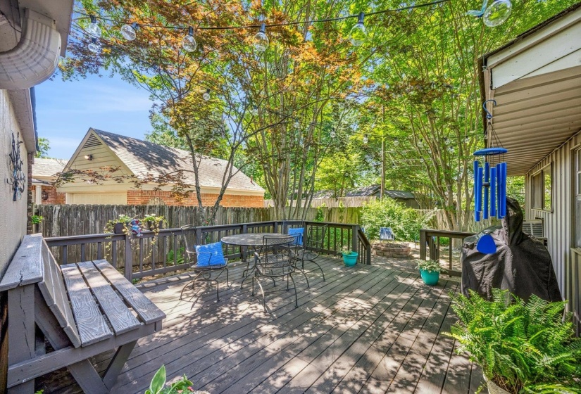 Spacious outdoor deck featuring wood flooring, a surrounding privacy fence, and mature trees providing natural canopy