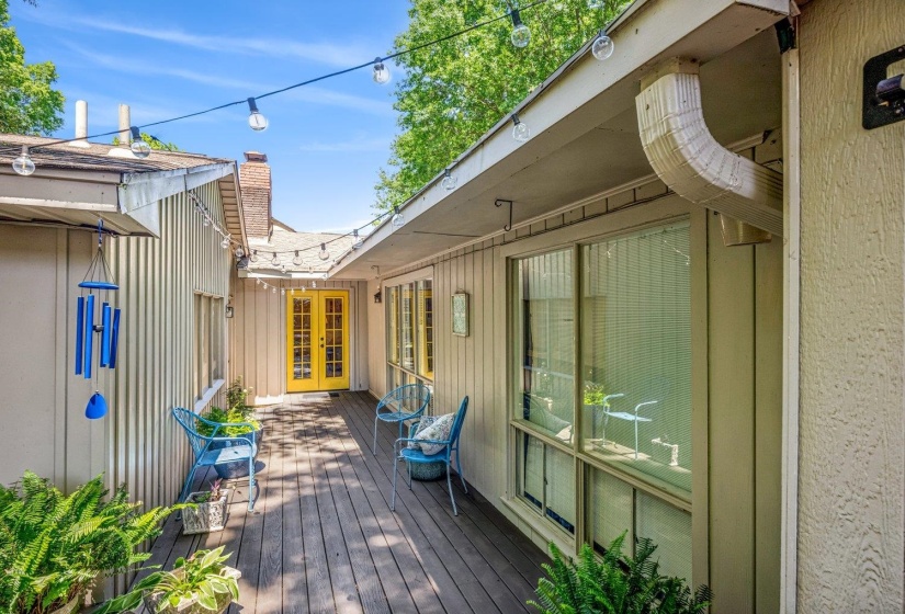 Outdoor decking with a vibrant yellow double door entry, board and batten siding, multiple windows, and integrated roof gutters