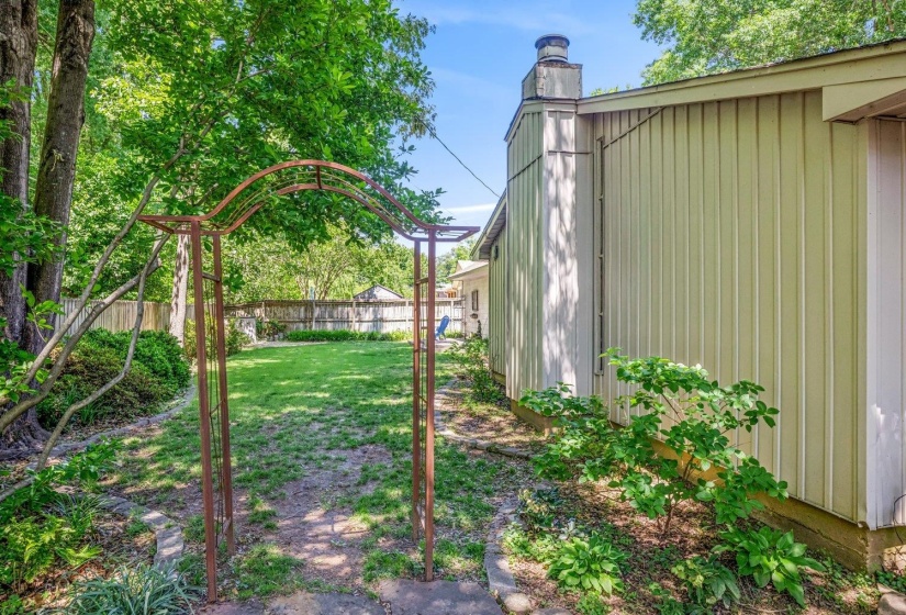 Expansive backyard featuring a lush lawn, mature trees, and a decorative metal archway