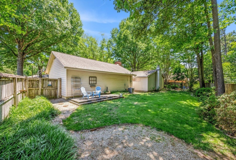 Expansive backyard featuring a stone patio, a manicured lawn, perimeter fencing, and mature trees