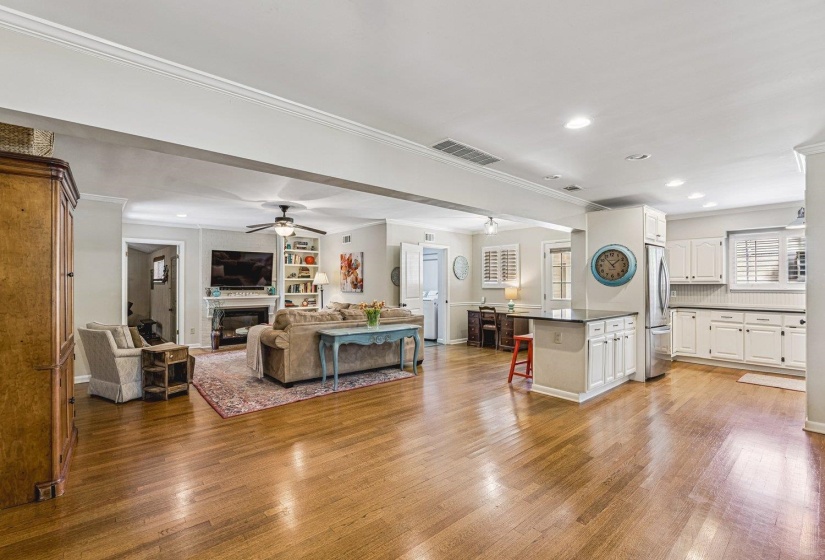 Expansive interior featuring wood-finish flooring, a white kitchen with stainless steel appliances, recessed lighting, crown molding, and a built-in bookshelf