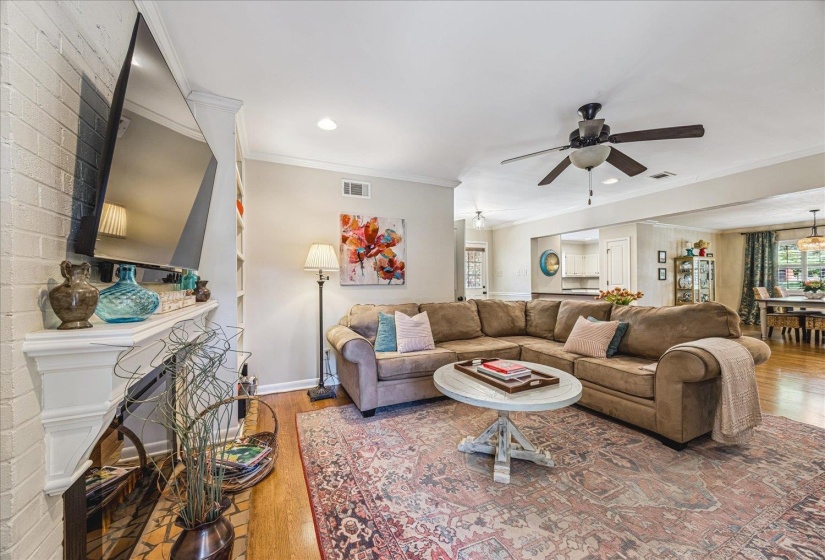 Living area featuring a white brick fireplace with a mantle, built-in shelving, wood-finish flooring, and a ceiling fan