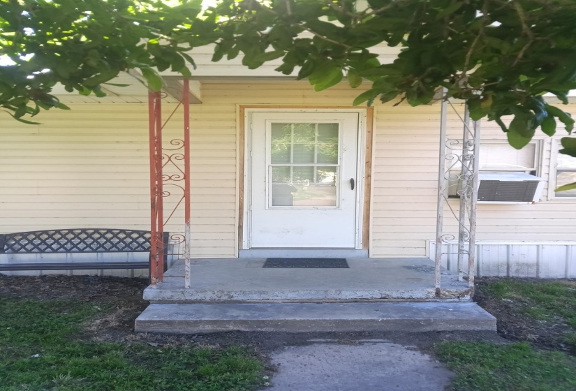 Front entryway featuring a white paneled door with windowpanes, concrete steps, and two decorative metal porch posts
