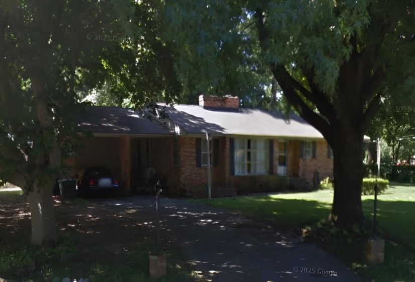 Brick facade home with mature front yard trees and a paved driveway leading to a covered carport
