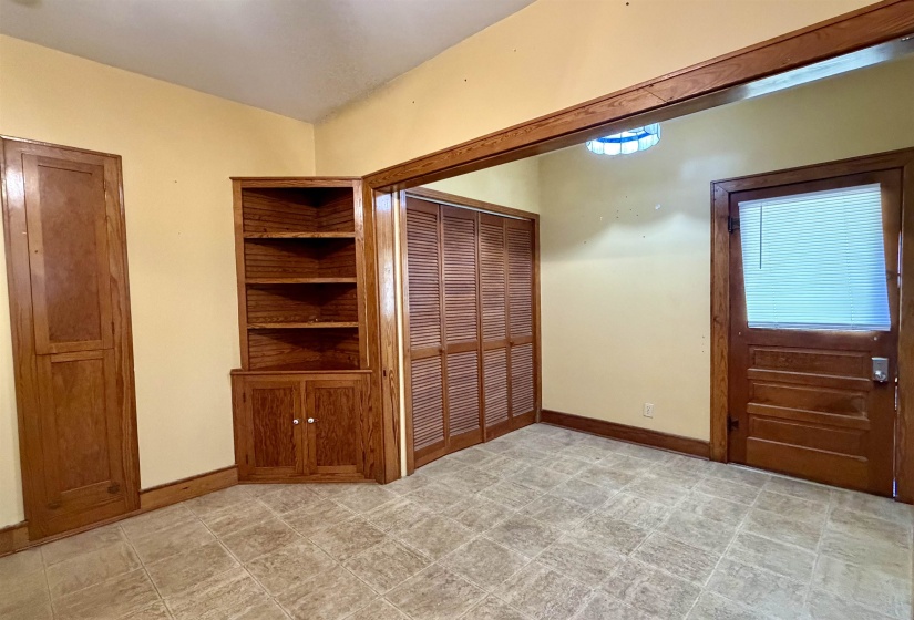 Room featuring wood-finish flooring, built-in wooden shelving with lower cabinetry, and louvered closet doors