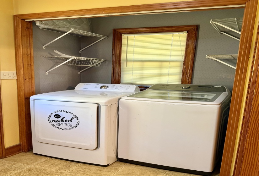 Dedicated laundry area featuring wire shelving, a window with blinds, and wood trim around the opening and window