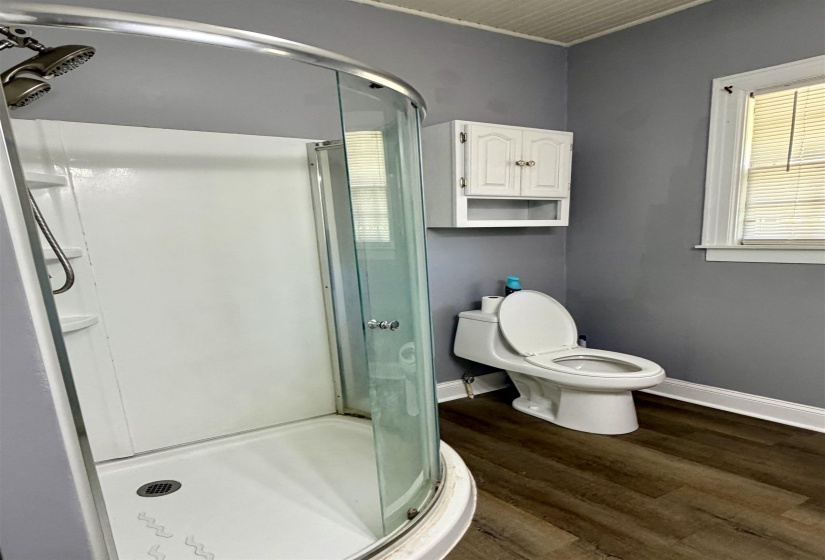 Bathroom featuring a corner shower enclosure with a clear glass door, wood-finish flooring, a white toilet, and a white wall-mounted cabinet