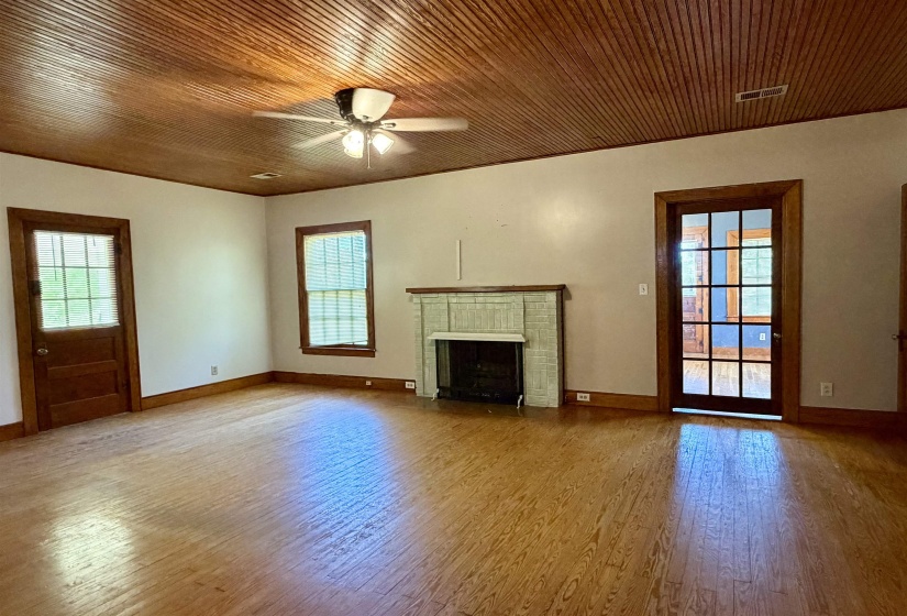 Spacious interior featuring wood-finish flooring, a beadboard ceiling with a ceiling fan, a fireplace with a stone surround, and multiple windows and doors with wood trim