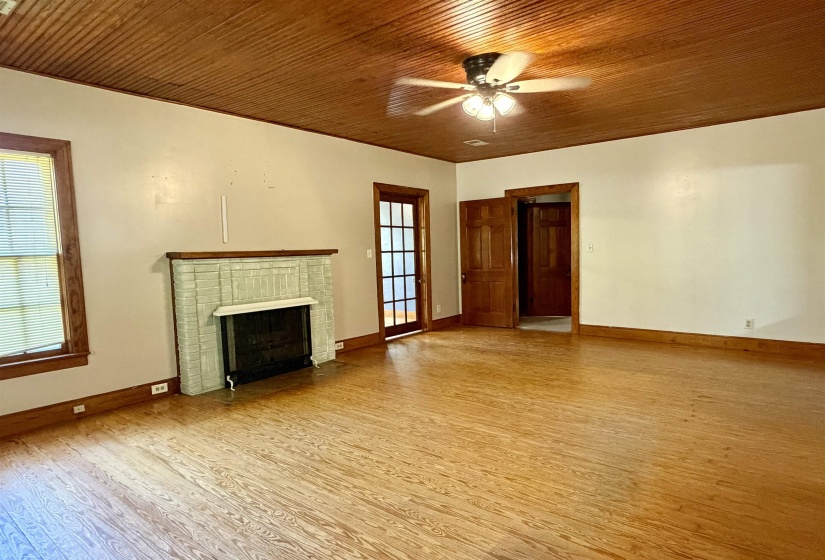 Spacious room featuring wood-finish flooring, a painted brick fireplace, a wood-paneled ceiling, and a ceiling fan with integrated lighting