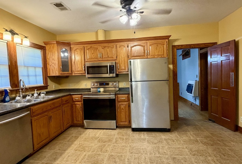 Kitchen featuring wood cabinetry, stainless steel appliances, dark countertops, and resilient flooring