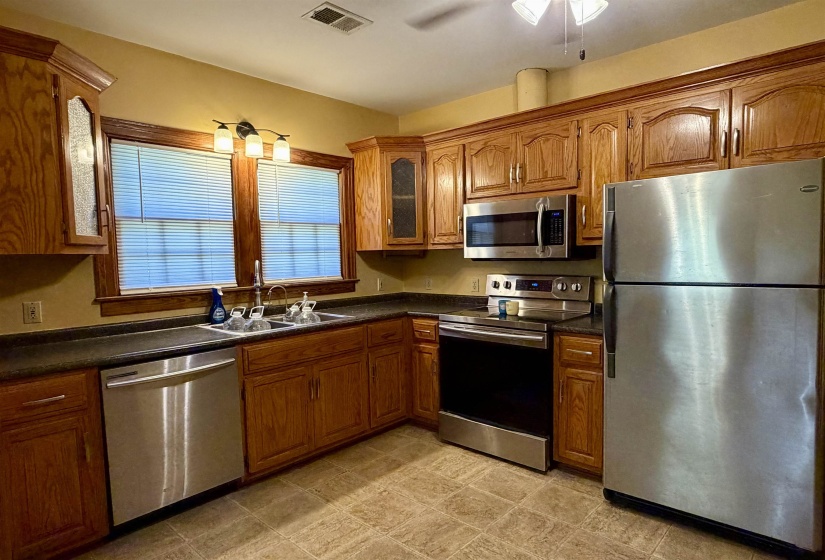Kitchen featuring wood cabinetry, stainless steel appliances, dark countertops, and ceramic tile flooring