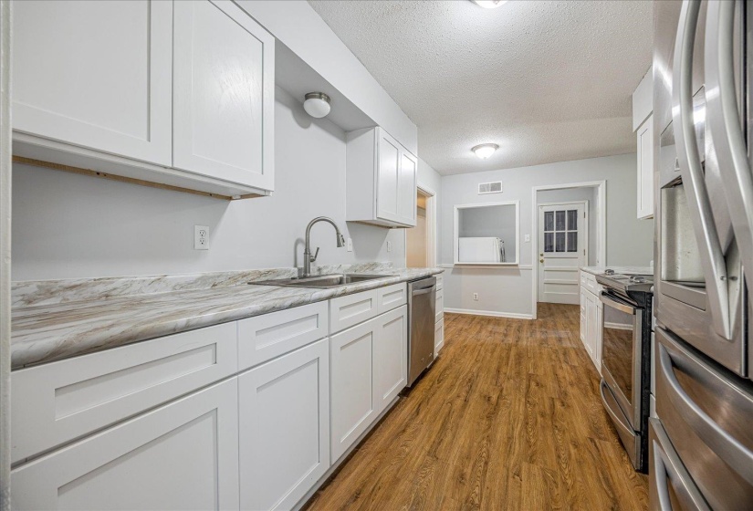 Kitchen with appliances with stainless steel finishes, a textured ceiling, dark wood-style floors, and white cabinetry