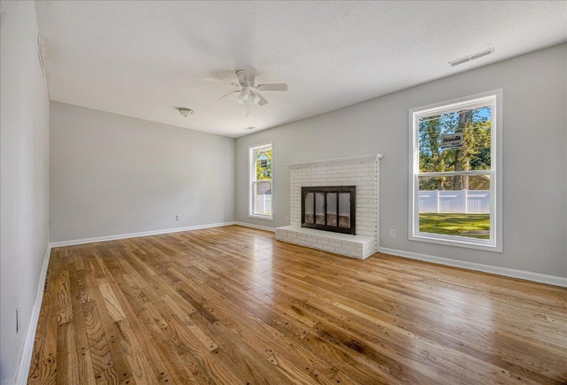 Unfurnished living room featuring a textured ceiling, light wood finished floors, ceiling fan, and a brick fireplace