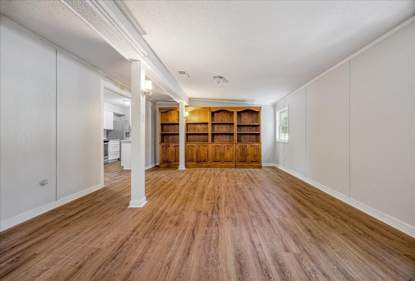 Unfurnished living room with a decorative wall, light wood-style floors, a textured ceiling, and crown molding