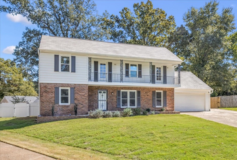 View of front of home with brick siding, concrete driveway, and a balcony