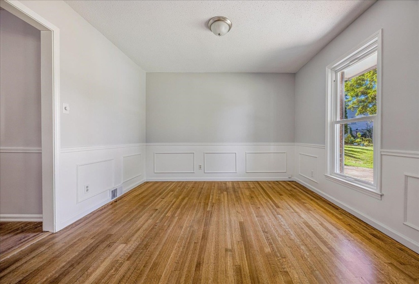 Unfurnished room featuring a decorative wall, wainscoting, light wood-style floors, and a textured ceiling