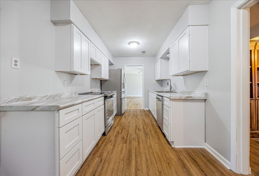 Kitchen with light wood-style flooring, a textured ceiling, light countertops, and appliances with stainless steel finishes
