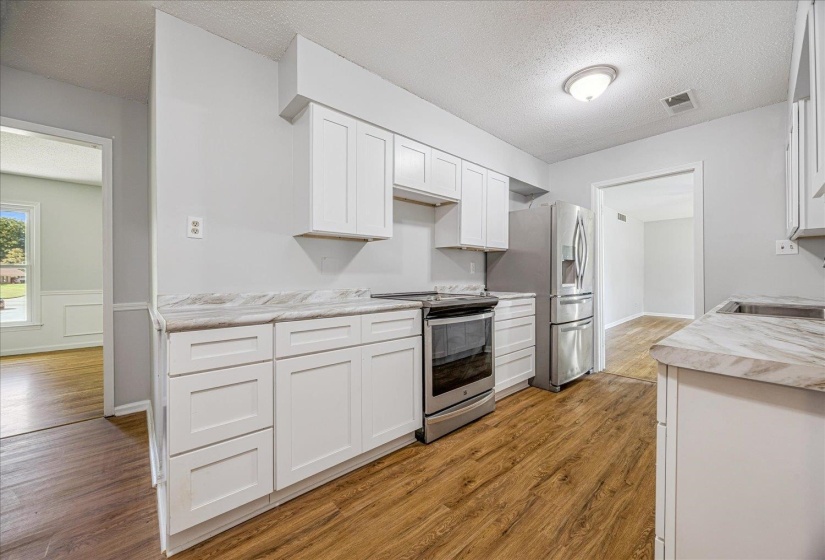 Kitchen with stainless steel appliances, light countertops, a textured ceiling, white cabinets, and a wainscoted wall