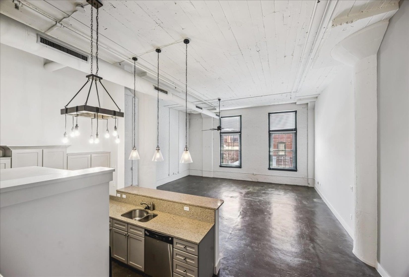 Open concept living area featuring high ceilings with exposed beams, polished concrete flooring, and multiple large windows