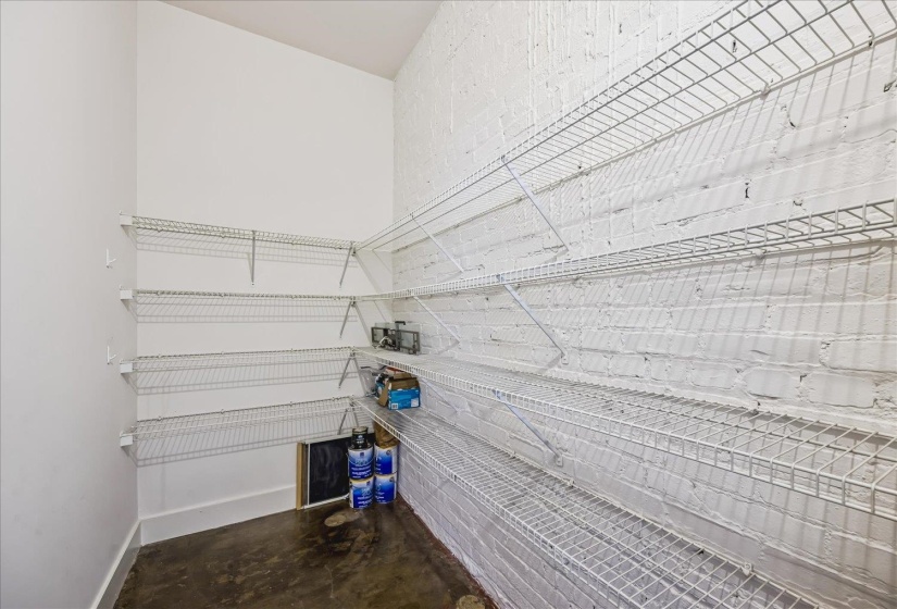 Storage area featuring white wire shelving, painted brick wall, angled ceiling, and concrete flooring